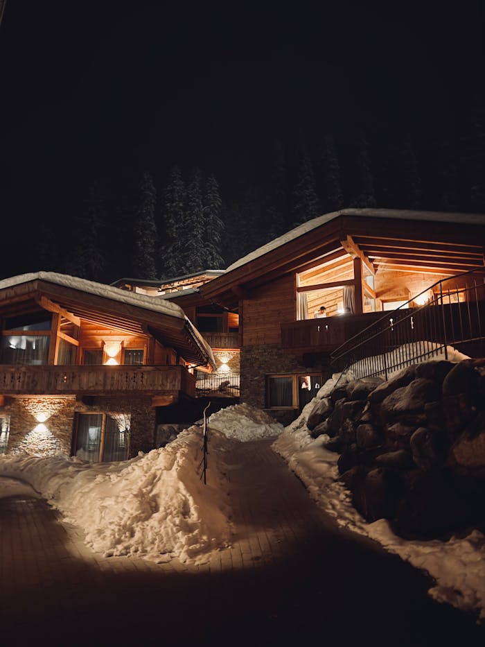 A wooden alpine chalet nestled in snowy mountains under the night sky.
